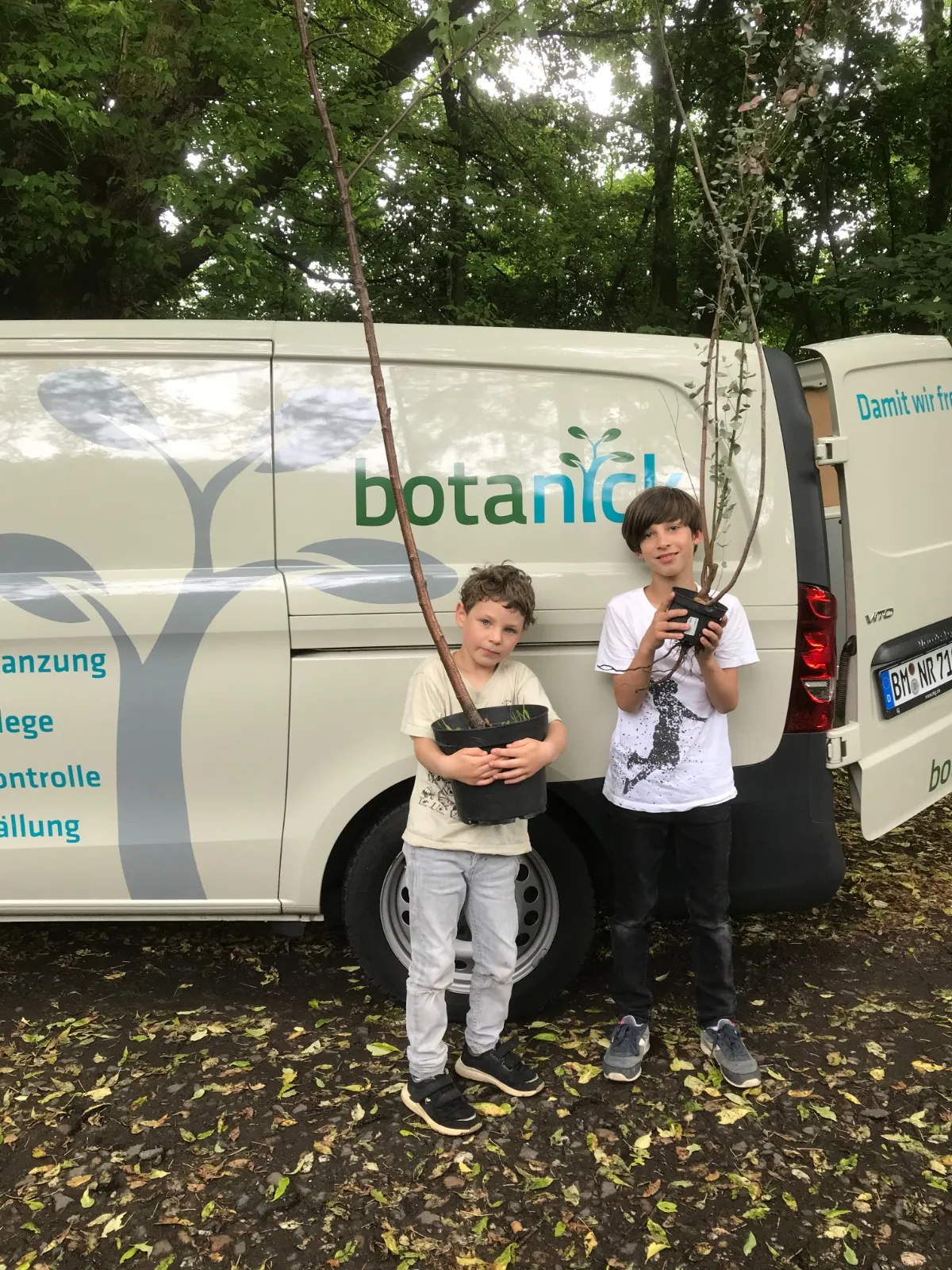 Zwei Kinder mit jungen Bäumen vor dem BotaNick-Fahrzeug